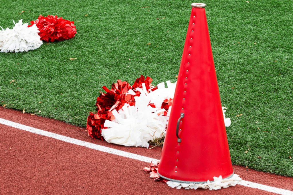 Red and white pom-poms and megaphone on the side of a football field.